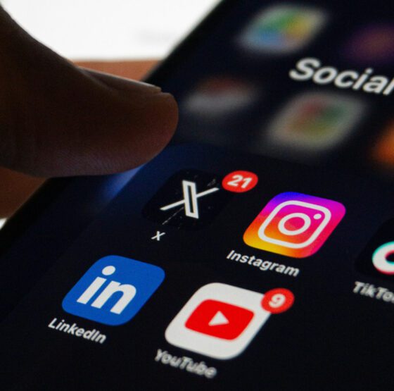 A small business owner looking at their smartphone, reviewing their social media feed with a thoughtful or frustrated expression, representing the challenge of building an audience without a clear content strategy.
