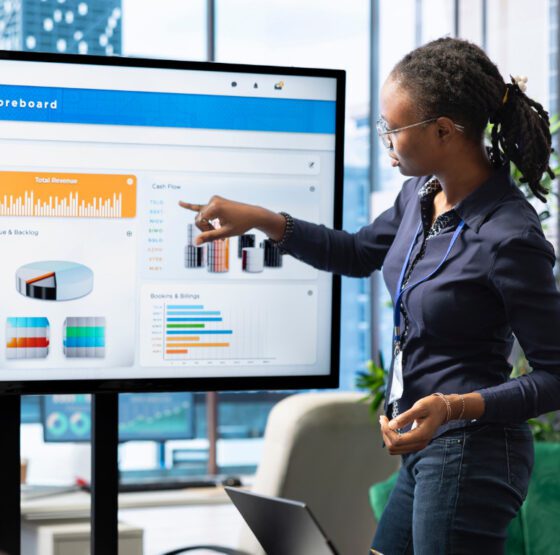 A professional woman presenting a financial executive Online Reputation Management scoreboard dashboard to colleagues in a modern boardroom, pointing at revenue and cash flow charts on a large screen illustrating a data-driven business performance review and strategic decision-making.