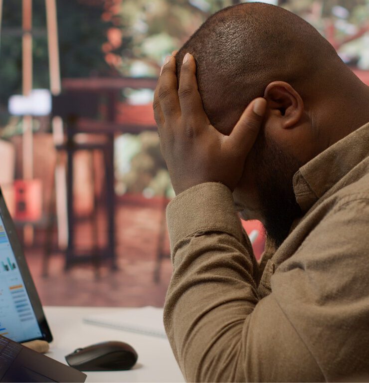 A frustrated business professional is sitting at a desk with a laptop and tablet displaying analytics social media dashboards, holding his head in his hands symbolizing the overwhelm of managing business growth without a clear digital marketing strategy.
